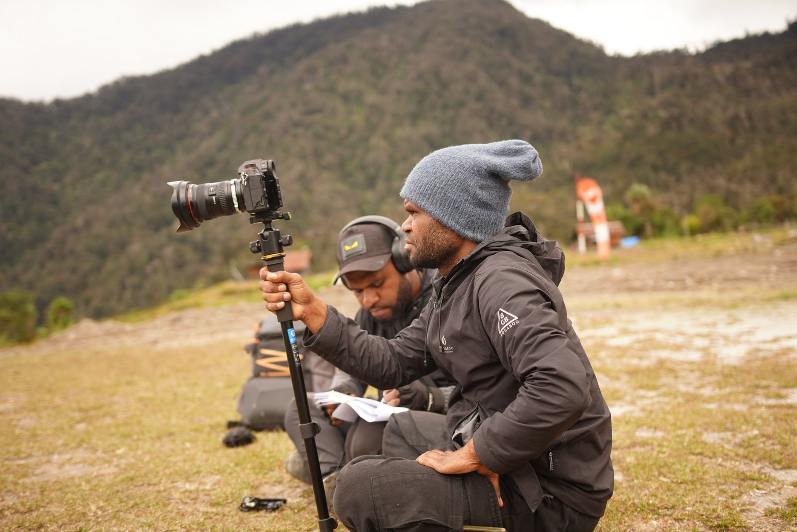 Two filmmakers preparing for a shoot in a picturesque mountain setting.