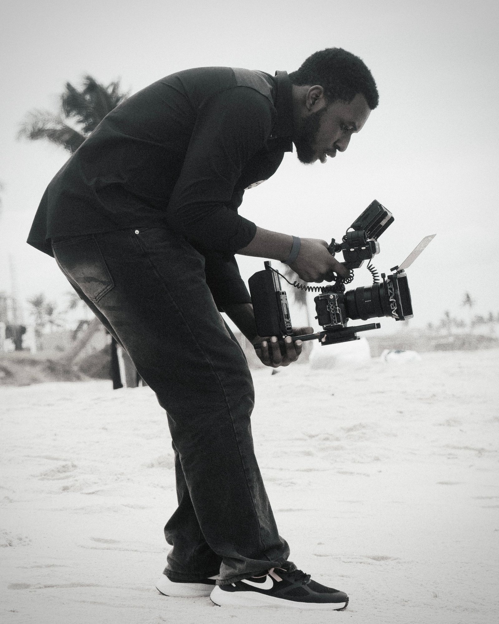 A videographer with camera equipment capturing footage on a sandy beach.